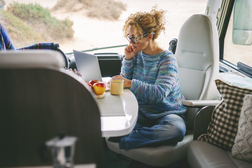 adult nice woman work on laptop sitting in a camper van dinette enjoying freedom travel vacation