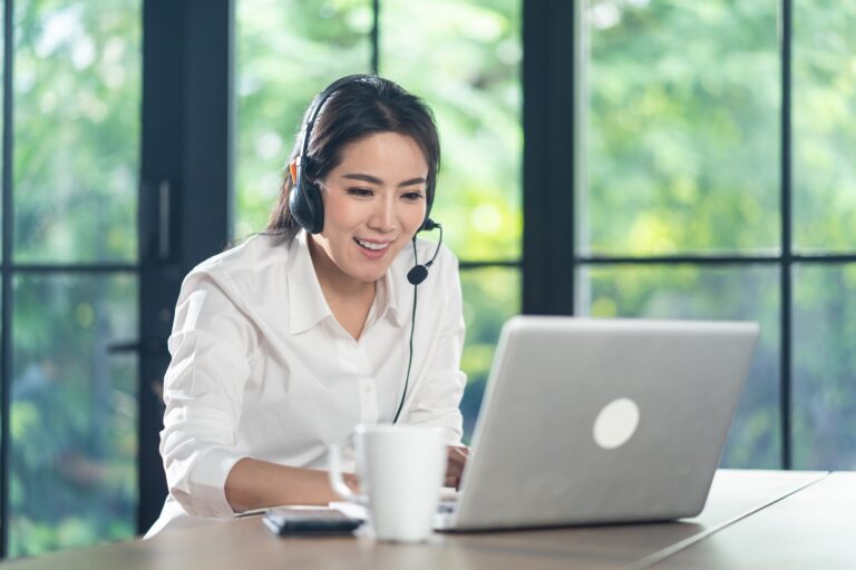 Asian Telemarketing or call center with headset working on computer lap top at home.