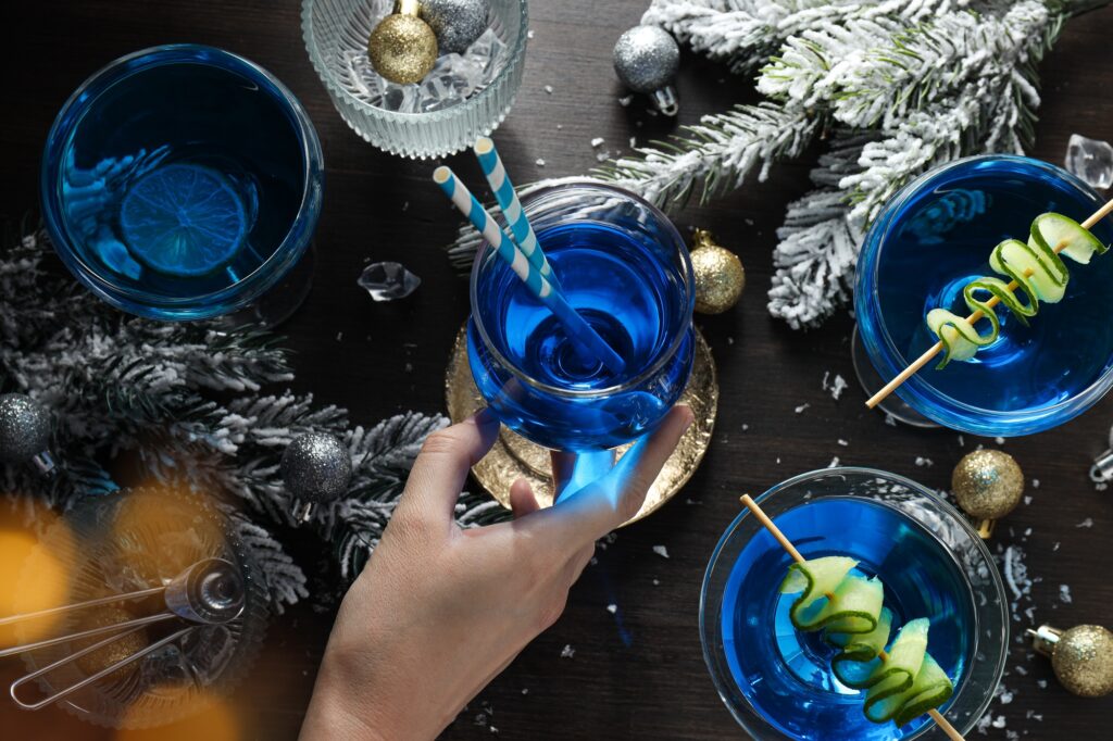 Blue cocktail in glasses, hand, christmas tree branches with snow and balls on wooden background